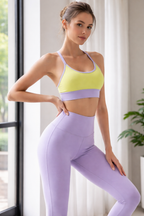 Woman wearing a yellow sports bra and purple leggings indoors.