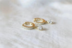 Gold hoop earrings with clear gemstones on a light fabric background