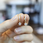 Gold earrings with small diamonds held between fingers against a blurred background