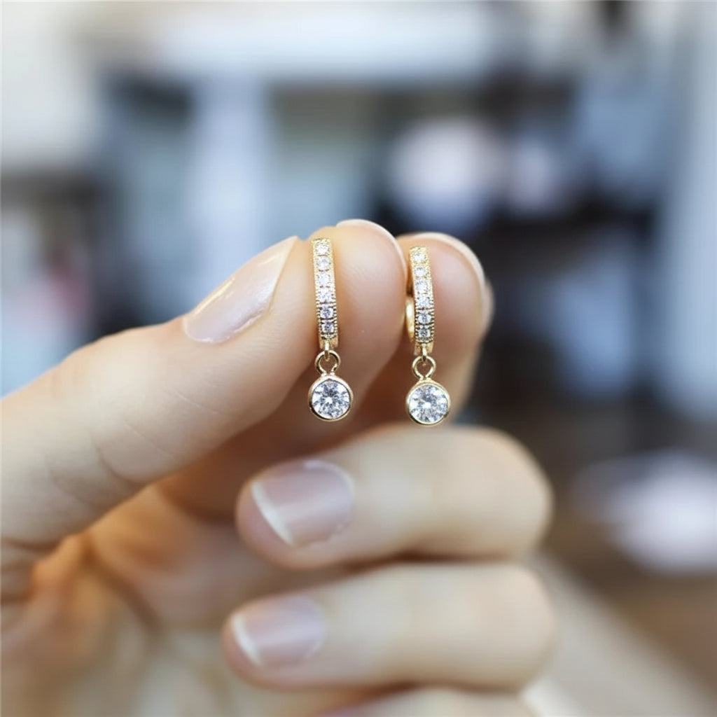 Gold earrings with small diamonds held between fingers against a blurred background