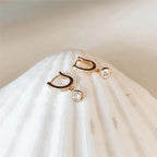 Pair of gold hoop earrings with clear gemstones on a white fabric background
