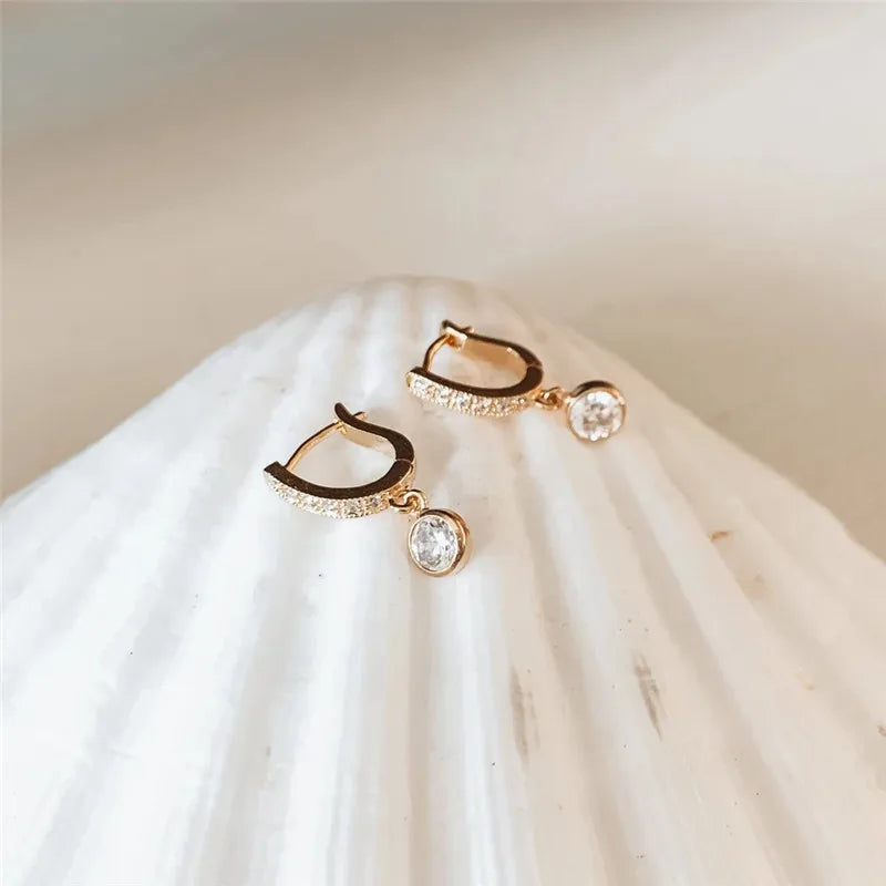 Pair of gold hoop earrings with clear gemstones on a white fabric background