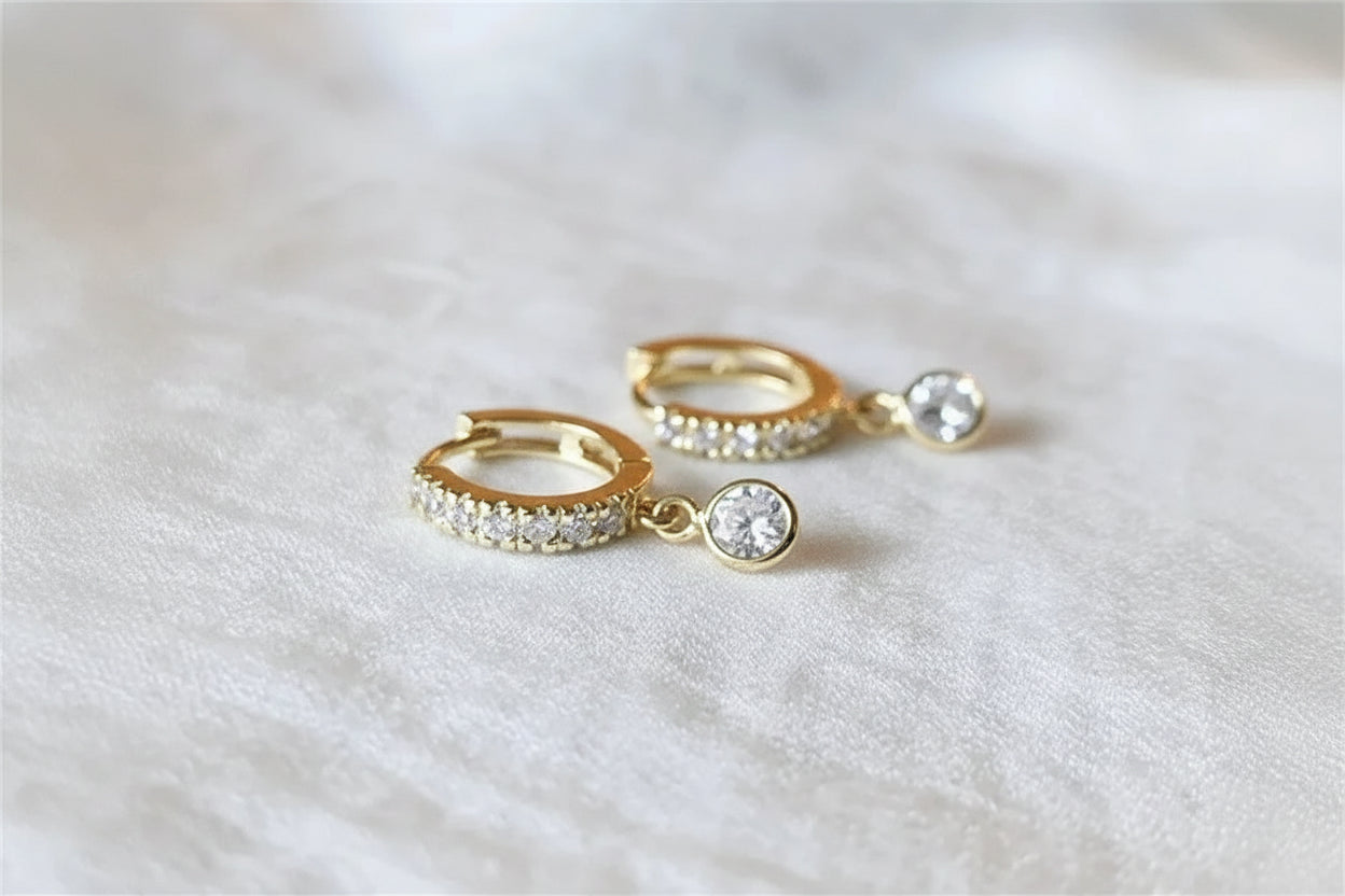 Gold hoop earrings with clear gemstones on a light fabric background