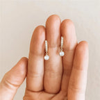 Diamond earrings held between fingers against a neutral background