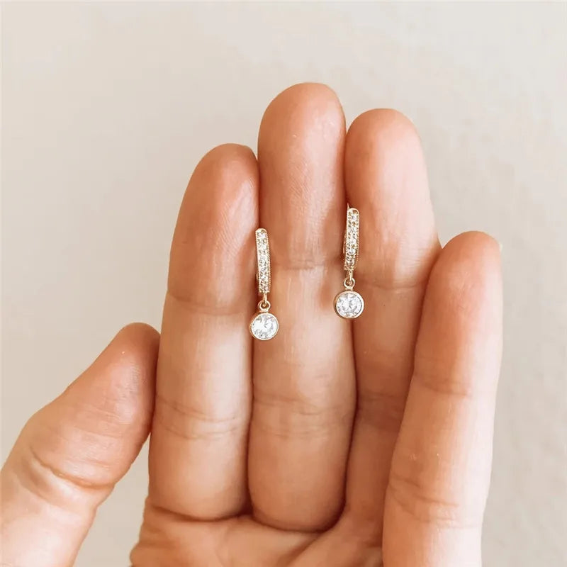 Diamond earrings held between fingers against a neutral background