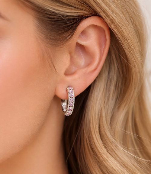 Close-up of a person wearing a silver hoop earring with clear stones.