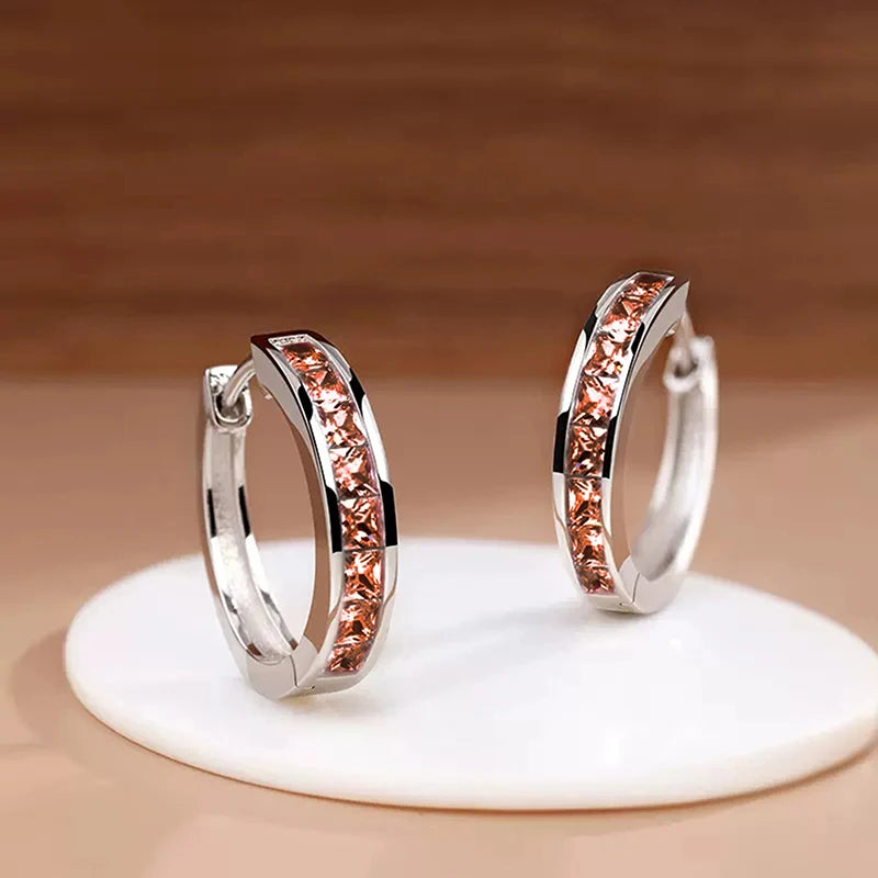 Pair of silver hoop earrings with rose gold accents on a beige stand.