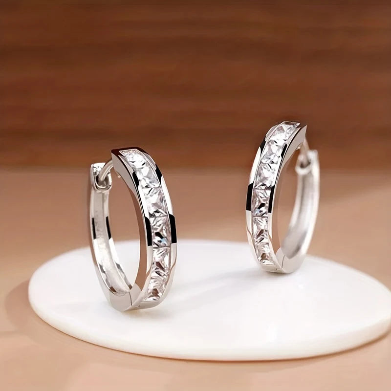 Pair of silver hoop earrings on a white stand with a wooden background