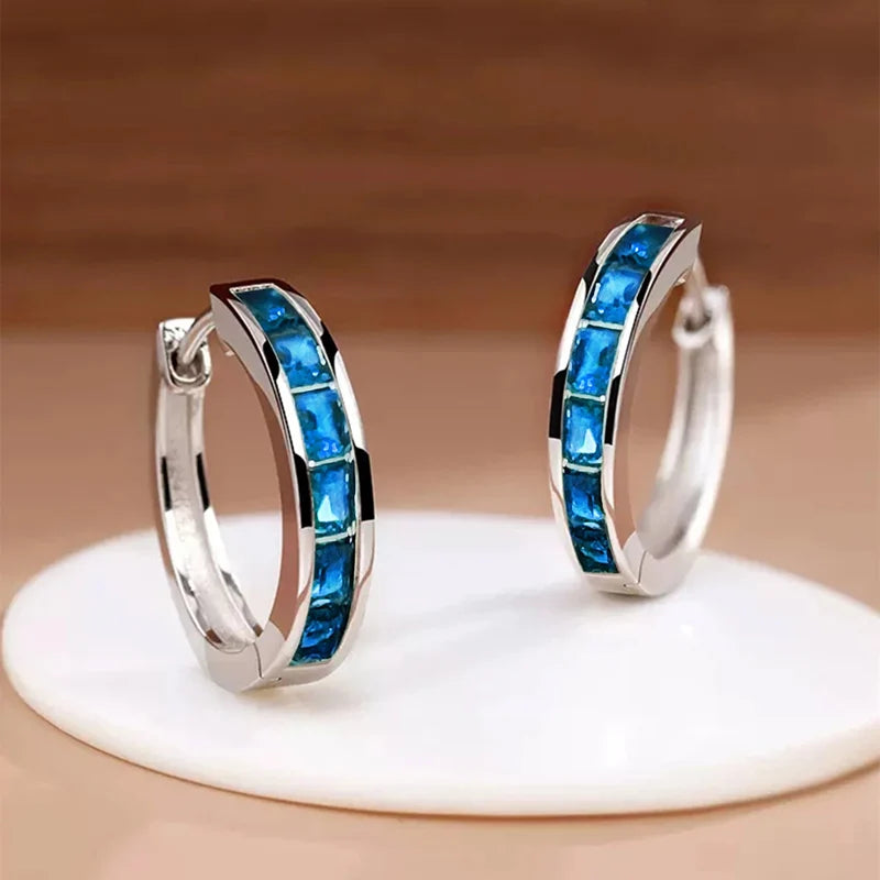 Silver hoop earrings with blue gemstones on a beige background