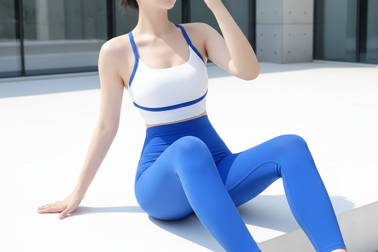 Person wearing a white top with blue straps and blue leggings sitting on a white surface.