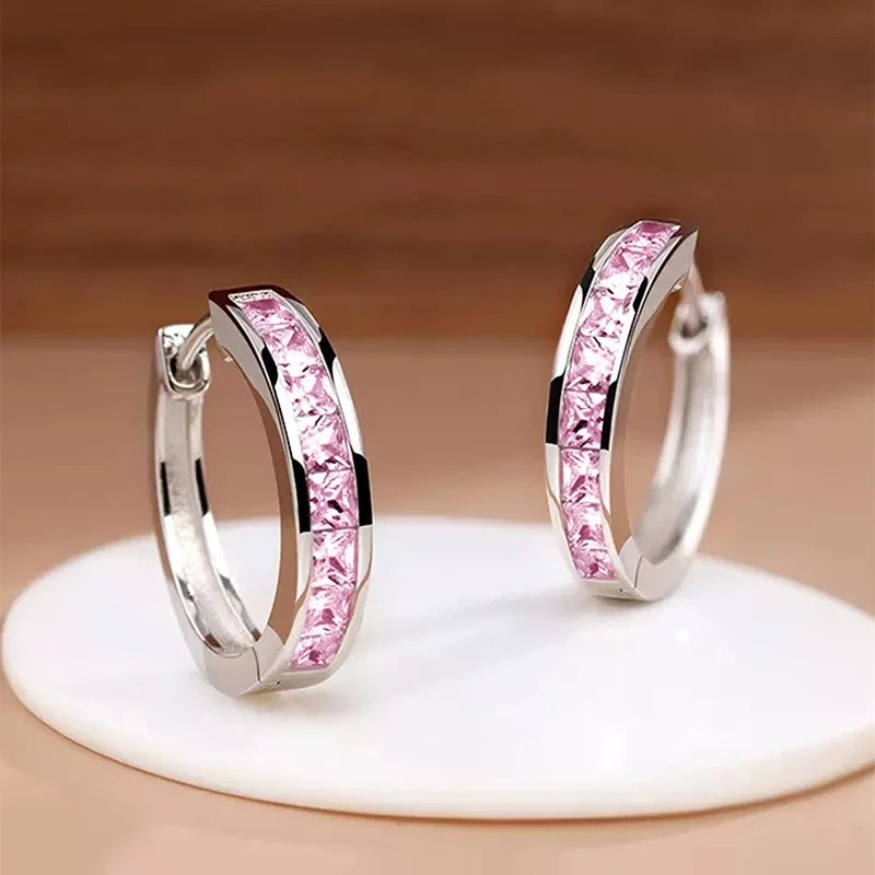 Silver hoop earrings with pink gemstones on a beige background