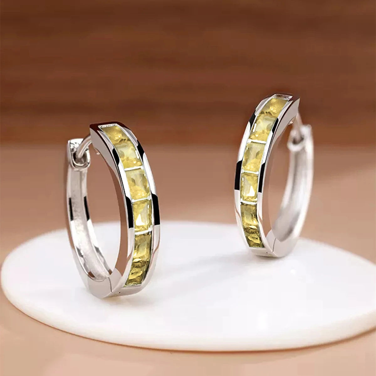 Pair of silver hoop earrings with yellow gemstones on a beige background